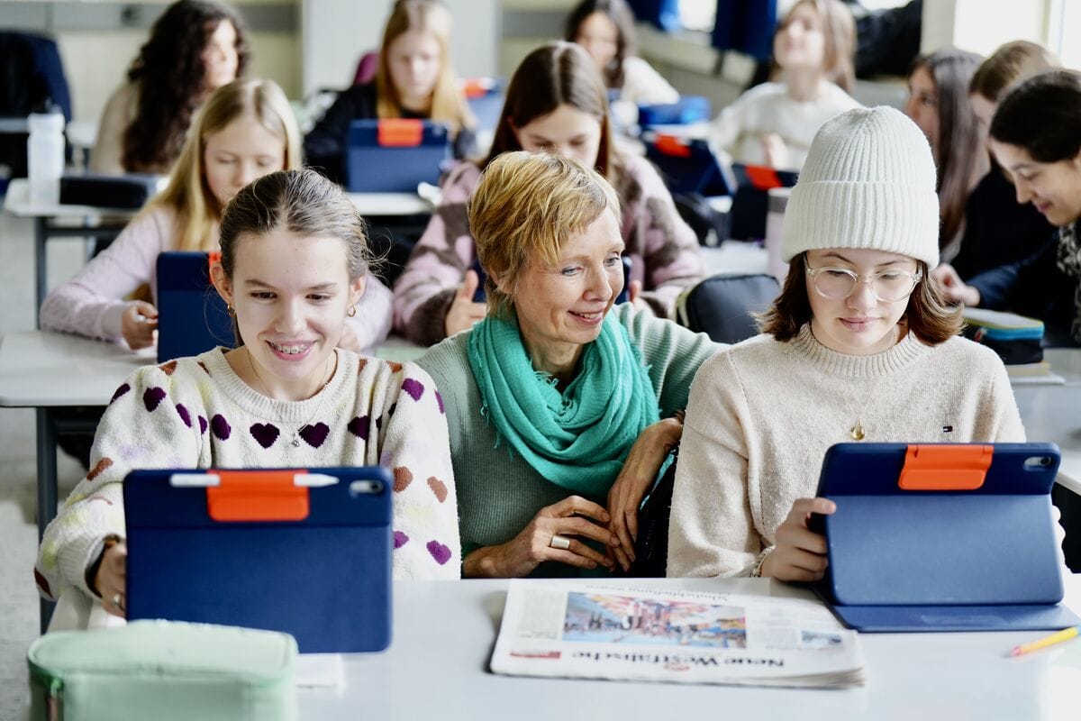 Schülerinnen arbeiten gemeinsam mit Tablets und einer Zeitung im Klassenzimmer