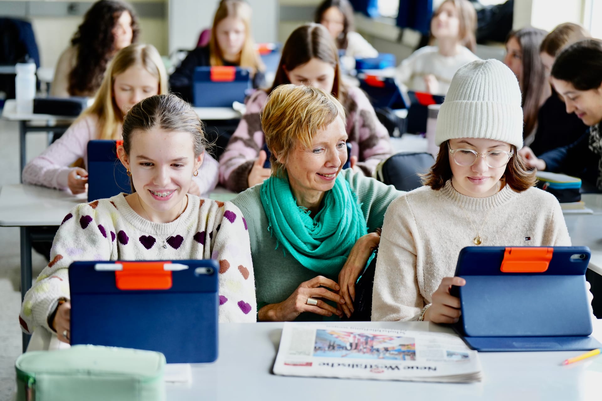 Lehrkraft arbeitet mit Schülerinnen an Tablets im Klassenzimmer